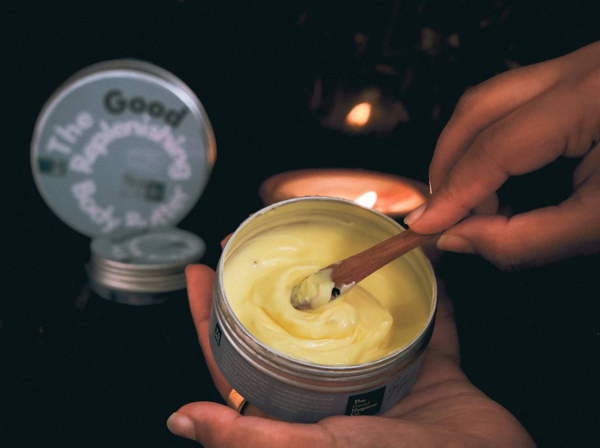 Hands mixing ingredients in a glass bowl for making cosmetic body lotion